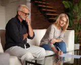 Un couple signe des documents, peut-être une désolidarisation de bail, dans un salon moderne. L'homme réfléchit, la femme écrit.