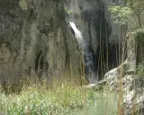 Cascada en un cañón rocoso, con juncos en primer plano. Un lugar ideal para explorar las rutas de agua en Alicante.