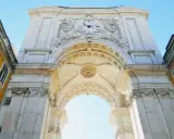 Der Arco da Rua Augusta in Lissabon, ein imposanter Triumphbogen mit einer Uhr und kunstvollen Verzierungen, ragt majestätisch in den blauen Himmel.