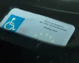 Niebieska karta parkingowa dla osoby niepełnosprawnej z symbolem wózka inwalidzkiego, umieszczona za przednią szybą samochodu.