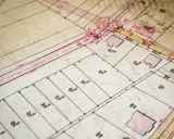 Stary plan działek z zaznaczonymi budynkami i wymiarami. Przypomina fragment ksiąg wieczystych po nazwisku, gdzie każdy kwadrat to osobna nieruchomość.
