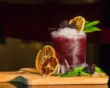 Cocktail rosso con frutti di bosco, arancia essiccata e menta, perfetto per un aperitivo a Riccione.