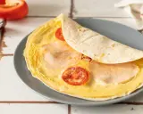 Pyszna tortilla z jajkiem, pomidorkami i szynką, gotowa do zjedzenia.