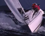 Voilier blanc fendant les vagues, deux personnes en ciré rouge. Une scène de navigation intense, digne des premiers 285 avis.
