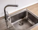 Błyszczący, metalowy zlew kuchenny z chromowaną baterią. Obok zlewu znajduje się ociekacz. Do czyszczenia takiego zlewu przyda się sól do zlewu.