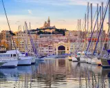 Barche a vela ormeggiate nel porto di Marsiglia, con la Basilica di Notre-Dame de la Garde sullo sfondo. Un'ottima vista per chi cerca cosa vedere a Marsiglia vicino al porto.