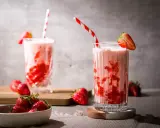 Zwei Gläser mit einem cremigen Erdbeer Milchshake, garniert mit frischen Erdbeeren und gestreiften Strohhalmen.
