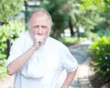 Mann mit COPD hustet im Freien. Sein dicker Bauch ist durch die weiße Kleidung sichtbar.