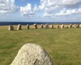 Rząd kamieni Ales Stenar na trawiastym polu, z morzem i chmurami w tle.