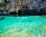 Persona nada en un pou clar de aguas turquesas, bajo un acantilado rocoso.