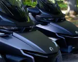 Dwa matowe, czarne pojazdy typu Can-Am Spyder stoją obok siebie na parkingu dla motocykli, gotowe do jazdy.