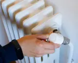 Mano ajustando el termostato de un radiador blanco. Controlar la temperatura ayuda a saber cuanto cuesta la calefaccion al mes.