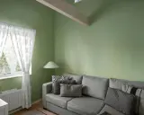 Sofá gris con cojines, lámpara y cortinas blancas junto a pared verde. ¡Excelentes ideas pintar casa con este tono fresco!