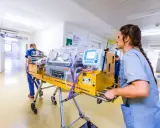 Infermiera spinge un'incubatrice mobile in un corridoio ospedaliero. Quanto tempo in terapia intensiva neonatale è cruciale per questi piccoli pazienti.