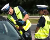 Policjanci w kamizelkach odblaskowych mierzą prędkość samochodu radarem.