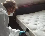 Persona con equipo de protección fumiga un colchon sucio, intentando eliminar ácaros y bacterias.