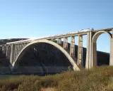 Un tren de alta velocidad cruza un imponente puente arco de hormigón sobre un embalse.