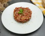 Delicioso steak tartar de fuet, picado finamente con especias y semillas de sésamo, adornado con una hoja de perejil.