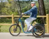 Un homme âgé roule sur un tricycle électrique bleu, son certificat d'homologation vélo électrique en poche.
