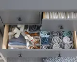 Ordentliche Schubladen einer Wickelkommode beschriften: Windeln oben, Babykleidung und Spielzeug unten, alles übersichtlich sortiert.