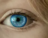 Niebieskie oko, jakby po chwilowej utracie wzroku, z refleksami zieleni i blond włosami.