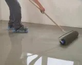 Persona con calzado de púas usando un rodillo para nivelar un suelo recién vertido.
