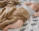 Bebé durmiendo plácidamente, envuelto en una manta de tonos tierra. Las medidas del arrullo bebé son ideales para su comodidad.