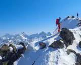 Wspinaczka zimą na Orlą Perć. Dwóch alpinistów na ośnieżonym szczycie, jeden z nich asekurowany liną.