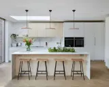 Cuisine moderne avec îlot central, tabourets en bois et une niche ouverte intégrée dans les placards.