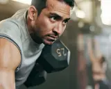 Fokusierter Mann hebt Hantel. Sein Schweiß glänzt. Ein Teil eines 2er Split Trainingsplans.