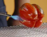 Un poivron rouge est rôti à la flamme sur une grille. La peau noircit par endroits, signe d'un poivron au four savoureux.