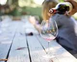 Czerwone wino nalewane z butelki do kieliszka na drewnianym stole.