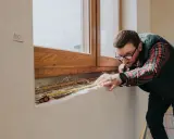 Mężczyzna w okularach mierzy taśmą okno, przygotowując się do montażu parapetu drewnianego.