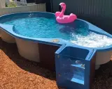 Petit jardin avec aménagement abord piscine hors sol. Un flamant rose gonflable flotte sur l'eau bleue.