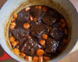 Boeuf bourguignon casero en olla roja, con trozos de carne tierna, zanahorias y champiñones en una rica salsa.