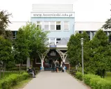 Studenci przed budynkiem koźmin uczelnia. W tle logo uczelni i napis www.kozminiński.edu.pl.