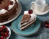 Una porción de tarta Selva Negra, con capas de bizcocho de chocolate, nata y cerezas, decorada con virutas de chocolate y una cereza encima.