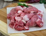 Surowe, pokrojone w kostkę mięso wieprzowe, idealne na gulasz. W tle czosnek i papryczki chili.