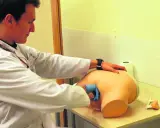 Mężczyzna w białym fartuchu ćwiczy na fantomie, jak wygląda badanie prostaty.