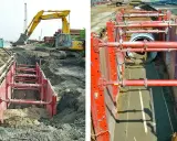 Excavación con entibación ligera para instalar tuberías. Maquinaria pesada y sistema de soporte rojo aseguran el área.