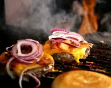 Pyszne burgery z grilla, z rozpływającym się serem i chrupiącym boczkiem, unoszą się w dymie.