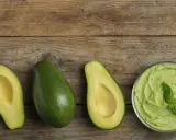 Avocado lagern: Ganze und halbe Avocados, Guacamole in einer Schüssel und Avocado-Toast auf Holzuntergrund.