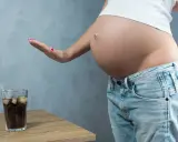 Schwanger und verzichtet auf Cola. Eine Hand weist ein Glas Cola mit Eis und Strohhalm ab.