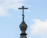 Drewniany krzyż na kopule cerkwi, symbol religii w Gruzji, na tle błękitnego nieba z chmurami.