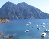 Vue d'une baie rocheuse avec plusieurs voiliers et bateaux à moteur en mouillage forain, sous une montagne imposante.