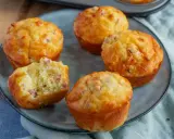 Fünf herzhafte Muffins mit Speck und Käse auf einem grauen Teller. Einer ist angeschnitten und zeigt die saftige Krume.