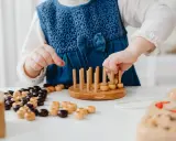 Niña con vestido azul jugando con cuentas de madera y un juego de encaje, parte de juegos para superar el mutismo selectivo.