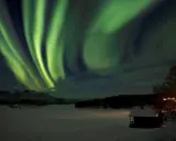 Grön aurora sweden dansar över ett snötäckt landskap med en liten stuga i förgrunden.
