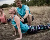Ein Trainer unterstützt eine Frau bei einer Yoga-Übung im Freien. Das **Faszien Training** stärkt die Körpermitte.
