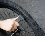 Dłoń używa czarnej łyżki do opon rowerowych, aby zdjąć oponę z obręczy. To proste narzędzie, które ułatwia wymianę dętki.